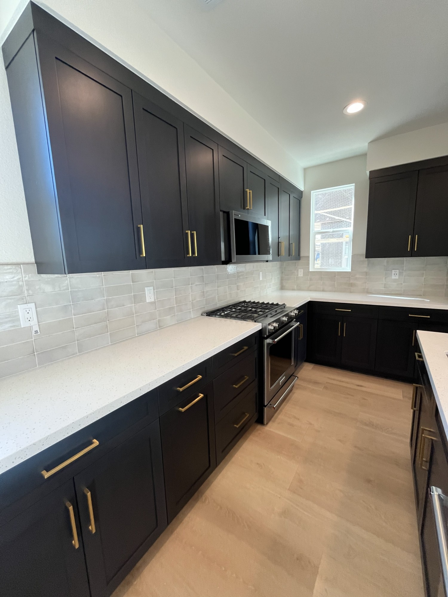 Dark shaker cabinetry with brass pulls, quartz counters and tile backsplash