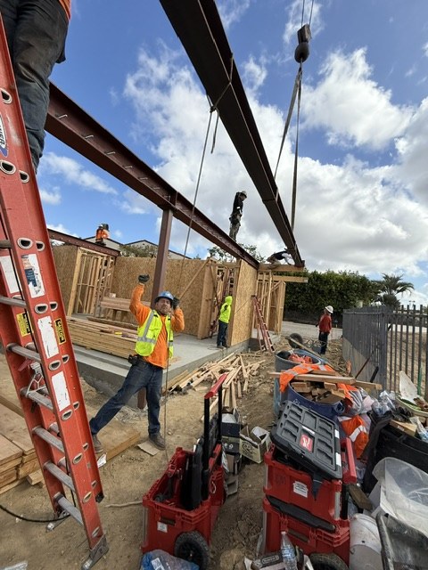 Crane setting a steel beam with crew below